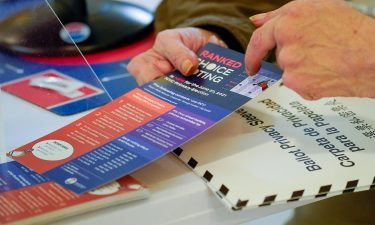 An election worker goes over a ranked choice voting explanation card with a voter before she casts her vote during early voting in the primary election