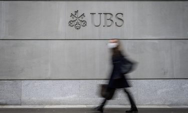 A pedestrian wearing a facemask walks by the logo of Swiss banking giant UBS engraved on the wall of its headquarters in Zurich on March 3.