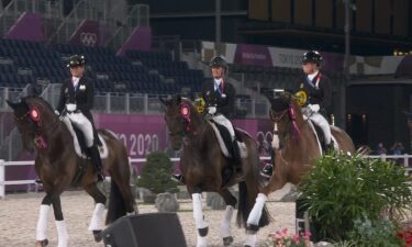 Three members of the German dressage team ride their horses in the arena with ribbons