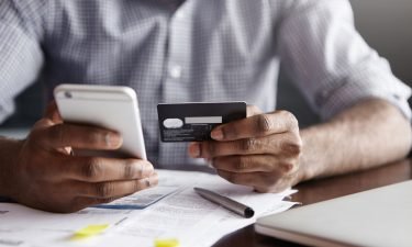 A man uses his phone and credit card to pay bills. Companies are beginning to give employees access to their paychecks before pay day.