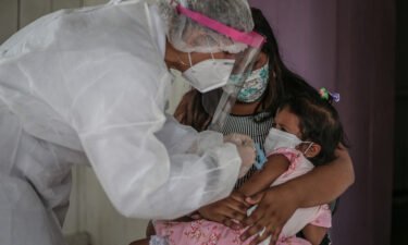 A mother in Brazil holds her daughter while a nurse gives her a flu vaccine.