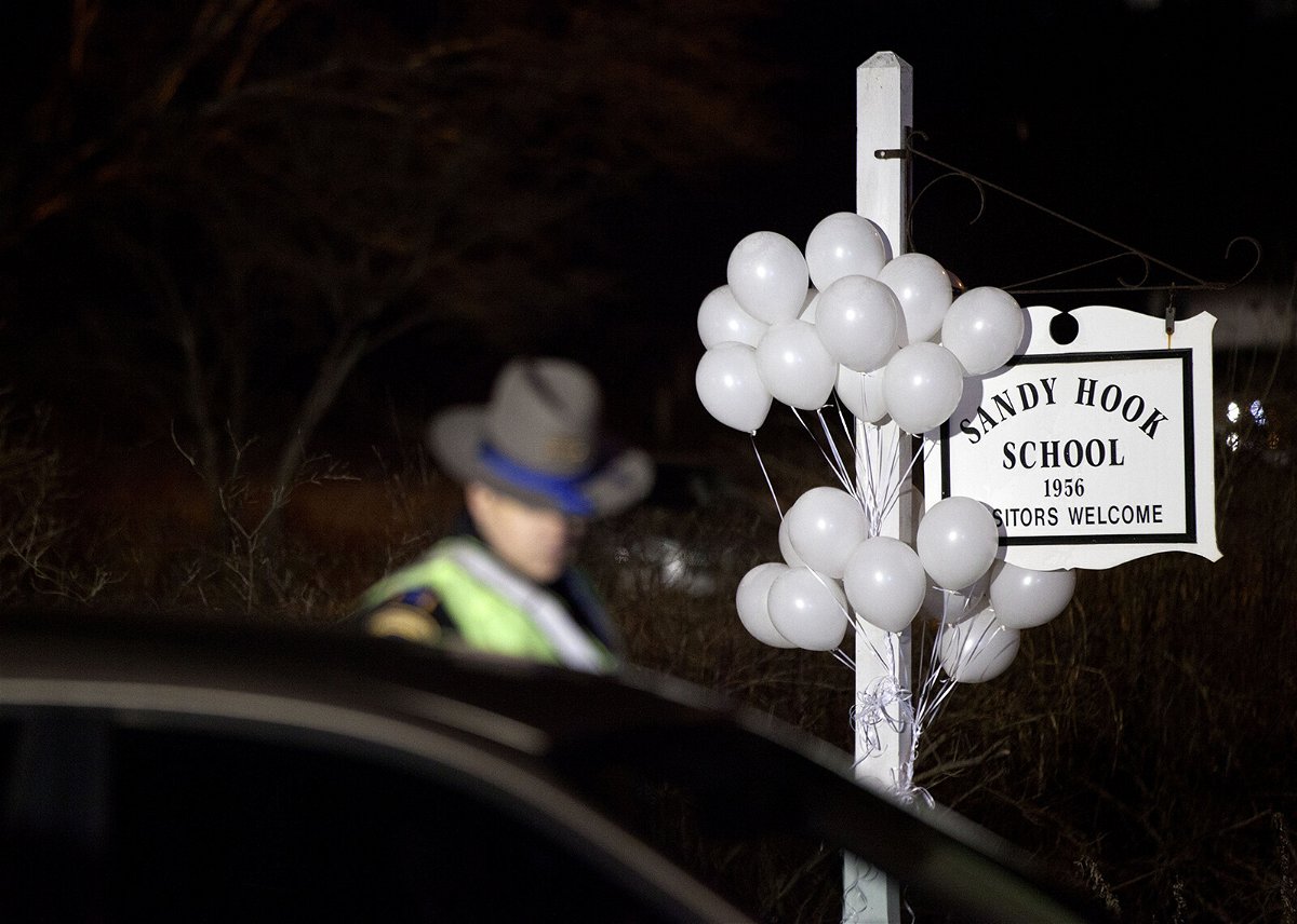 <i>David Goldman/AP</i><br/>White balloons decorate the sign for the Sandy Hook Elementary School as a Connecticut State Trooper stands guard at the school's entrance in 2012 in Newtown