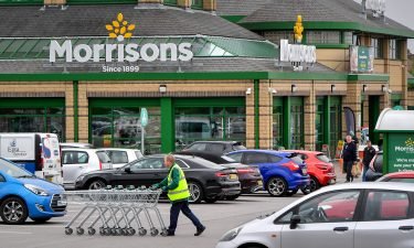 A worker pushes shopping trolleys through a Morrisons supermarket parking lot near the company's head offices in Bradford