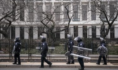 US Capitol police officers in protective riot gear walk by the fenced perimeter of the U.S. Capitol grounds in Washington