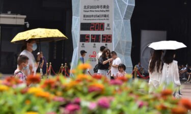 People wearing face masks walk past the countdown clock showing 200 days to the 2022 Olympic Winter Games.