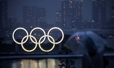 A woman walks past the Olympic Rings lit up at dusk in the rain