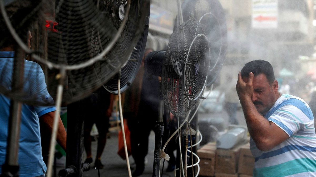 <i>AHMAD AL-RUBAYE/AFP via Getty Images</i><br/>A man stands by fans spraying mist along a street in Iraq's capital