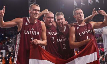 Four Latvian basketball players hold up the Latvian flag in celebration