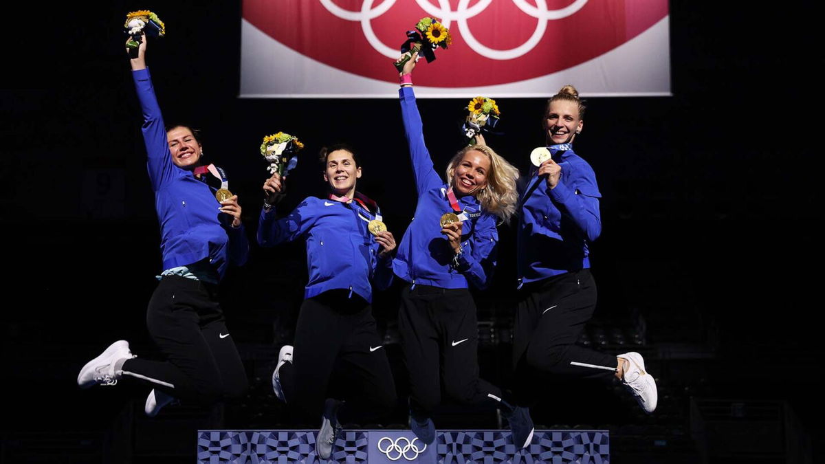 Four Estonian fencers jump in the air in celebration holding flowers and gold medals