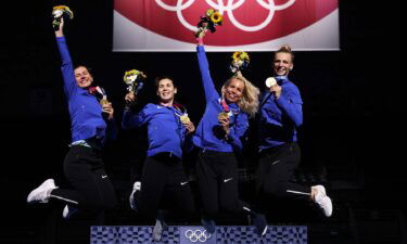 Four Estonian fencers jump in the air in celebration holding flowers and gold medals