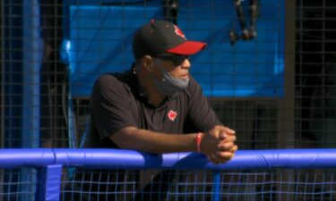 A man in a hat with a Canadian maple leaf printed on it stands next to a fence and leans over the top of it with his forearms.