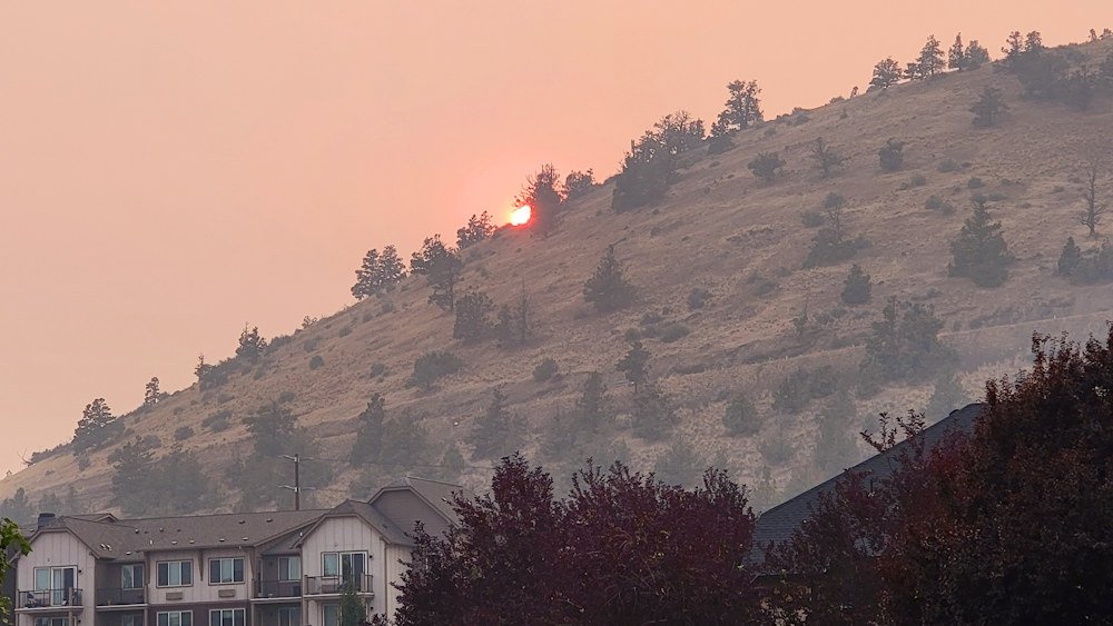 Sun sinks behind a smoke-shrouded Pilot Butte Tuesday evening, August 3