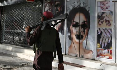 A Taliban fighter walks past a beauty saloon with images of women defaced using a spray paint in Kabul on August 18.