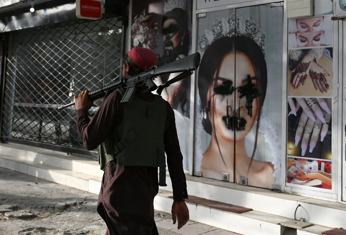 <i>Wakil Kohsar/AFP via Getty Images</i><br/>A Taliban fighter walks past a beauty saloon with images of women defaced using a spray paint in Kabul on August 18.