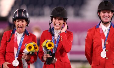 Three riders in red jackets stand smiling and wearing silver medals