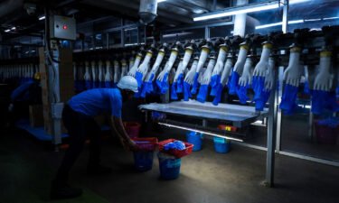 An employee monitors latex gloves on hand-shaped molds moving along an automated production line at a Top Glove factory in Selangor
