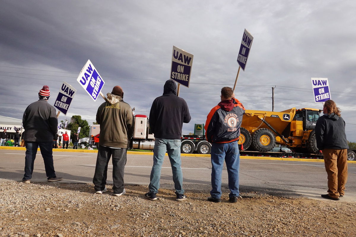<i>Scott Olson/Getty Images North America/Getty Images</i><br/>At truck hauls a piece of John Deere equipment from the factory past workers picketing outside of the John Deere Davenport Works facility on October 15 in Davenport