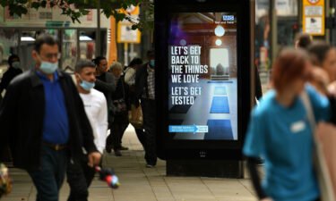 Pedestrians walk past an electronic display board promoting the "Test and Trace" coronavirus tracking scheme in Manchester