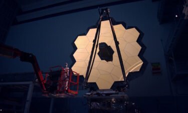 The James Webb Space Telescope primary mirror illuminated in a dark cleanroom.