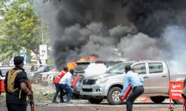 People extinguish fire on cars caused by a bomb explosion near Parliament building in Kampala