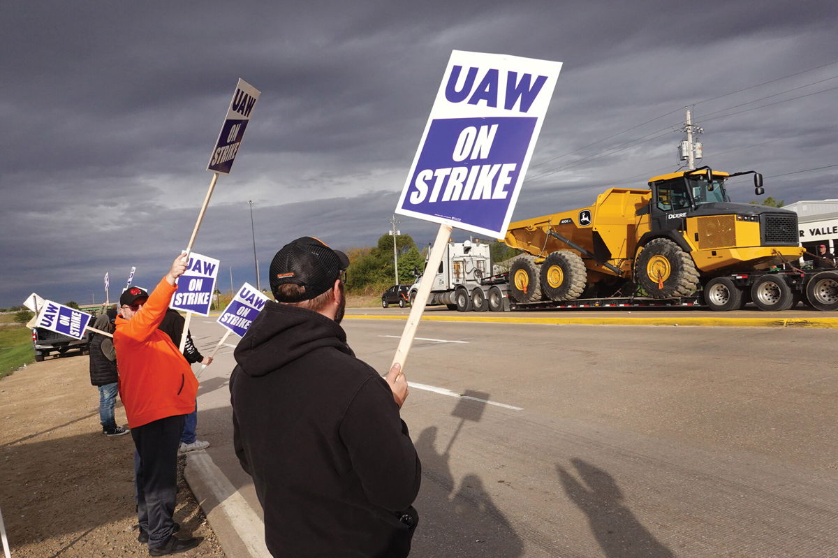 <i>Scott Olson/Getty Images</i><br/>At truck hauls a piece of John Deere equipment from the factory past workers picketing outside of the John Deere Davenport Works facility on October 15