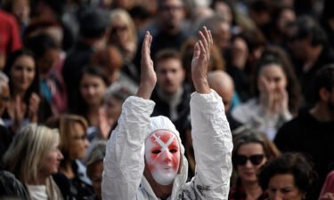 A protester wearing a mask depicting syringes and a full protection suit applauses in Geneva on October 9.