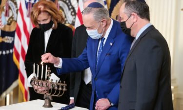 Senate Majority Leader Chuck Schumer lights a menorah as second gentleman Doug Emhoff looks on during a celebration of Hanukkah in the East Room of the White House on Wednesday