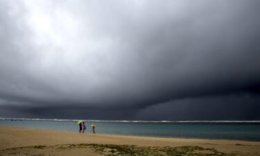 People hold umbrellas as it begins to rain on an otherwise empty beach in Honolulu on Dec. 6.
