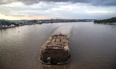 A barge filled with logged timber pulled along the Mahakam river passes the town of Samarinda