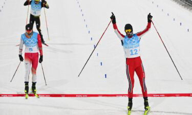 Norway's Joergen Graabak (R) celebrates as he crosses the finish line to win the cross-country race of the Nordic Combined men's individual large hill/10km event during the Beijing 2022 Winter Olympic Games