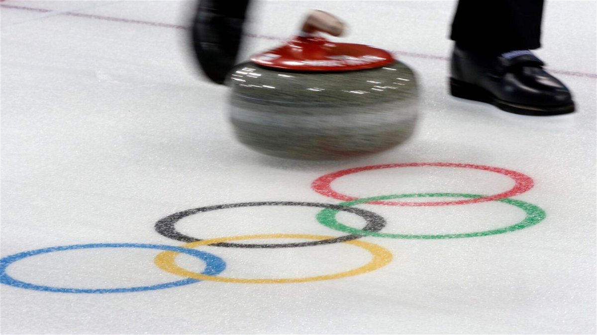A curling stone moves past the Olympic rings logo.