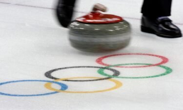 A curling stone moves past the Olympic rings logo.