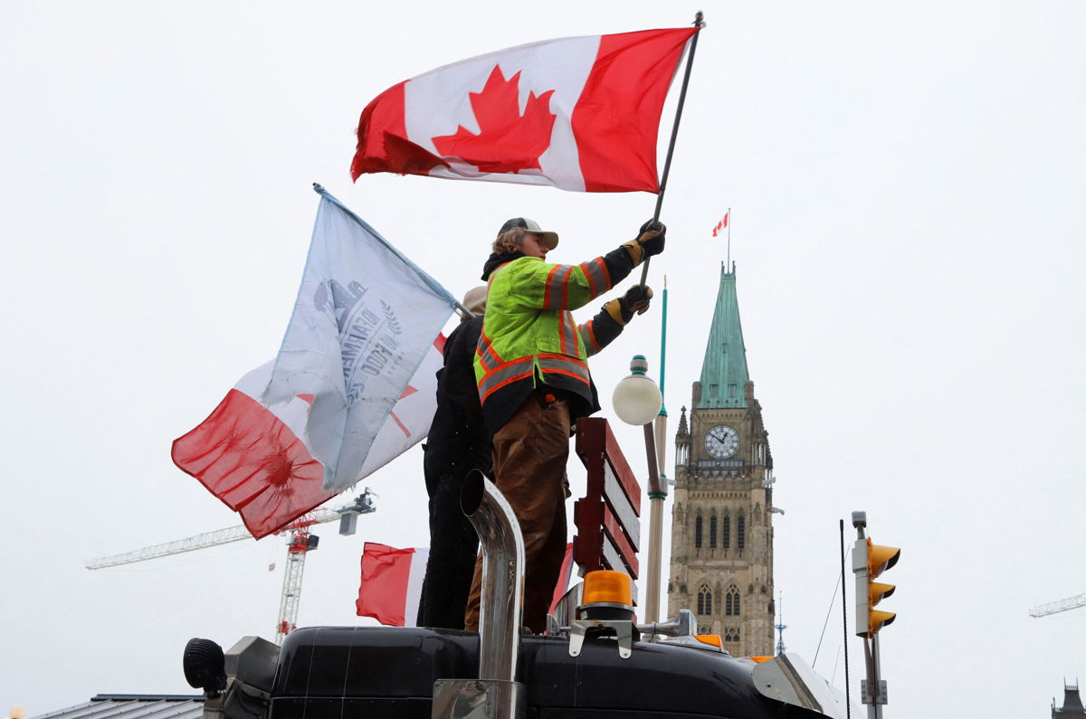 <i>Patrick Doyle/Reuters</i><br/>People wave flags on top of a truck in front of Parliament Hill on Sunday as truckers and their supporters continue to protest against the Covid-19 vaccine mandates in Ottawa.