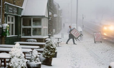 A local butcher carries his shop sign across a snowy pavement in  County Durham