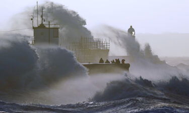 Waves crash against the sea wall and Porthcawl Lighthouse in Bridgend