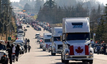 Trucks with Canadian flags drive by anti-vaccine mandate and anti-government protesters Saturday in Surrey