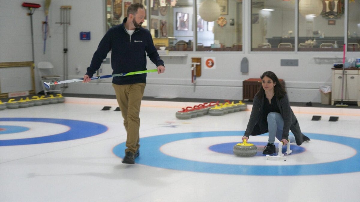 Katie Nolan throws yellow curling stone as Tyler George walks with curling broom