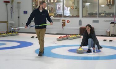 Katie Nolan throws yellow curling stone as Tyler George walks with curling broom