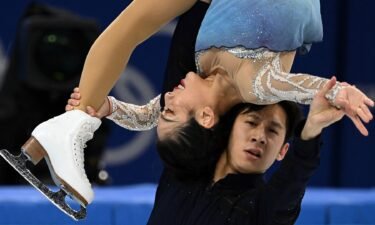 Han Cong in black lifts Sui Wenjing in blue and white above his head as she holds her ankle in front of her face