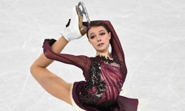 Anna Shcherbakova in dark red skates with arms up and leg back