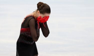 Emotional Kamila Valieva in black and red gloves with hands on face