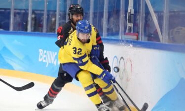 Swedish men's hockey player drives puck away from Canadian player