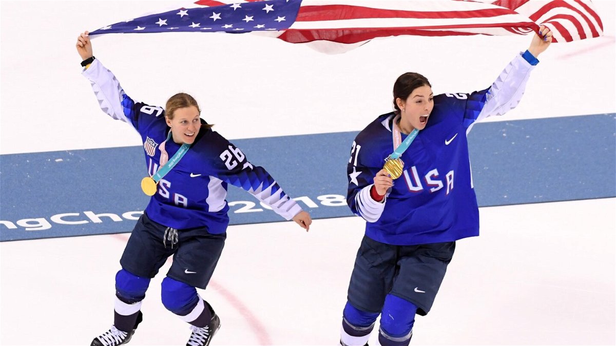 Two members of the U.S. women's hockey team celebrate by skate while holding up the U.S. flag and their PyeongChang gold medals