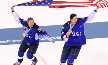 Two members of the U.S. women's hockey team celebrate by skate while holding up the U.S. flag and their PyeongChang gold medals