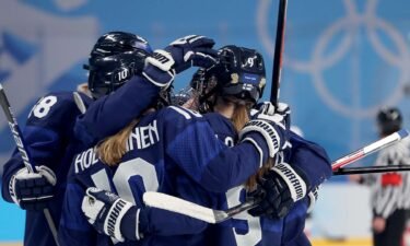 Three Finnish women's hockey players hug in celebration while on the ice