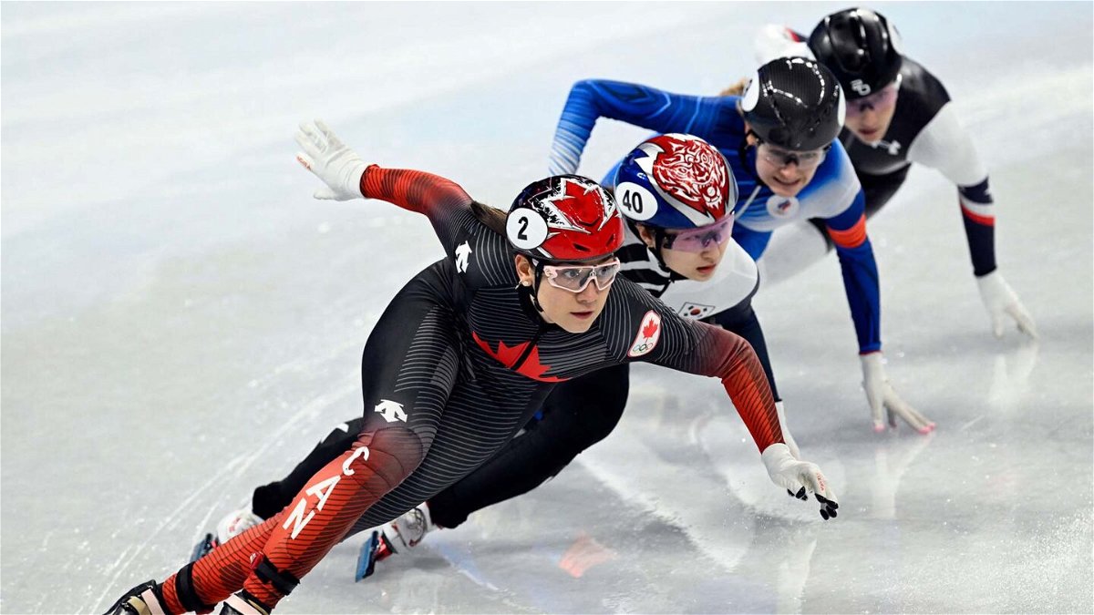 Four short track speed skaters crouch down and lean into a turn while skating
