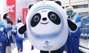 Panda mascot Bing Dwen Dwen stands in front of snowy Olympics venue