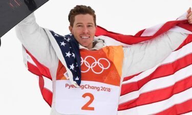 Shaun White holds his snowboard in the air while wearing an American flag