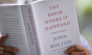A person is shown reading John Bolton's book "The Room Where it Happened."
