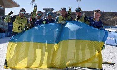 Ukrainian athletes celebrate with their country's flag after winning the mens middle distance vision impaired para biathlon.